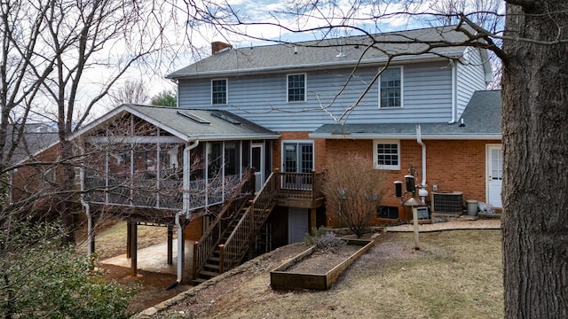 rear view of property featuring stairway, a sunroom, a chimney, a shingled roof, and brick siding