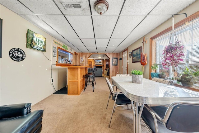 dining area featuring bar, a paneled ceiling, and light colored carpet