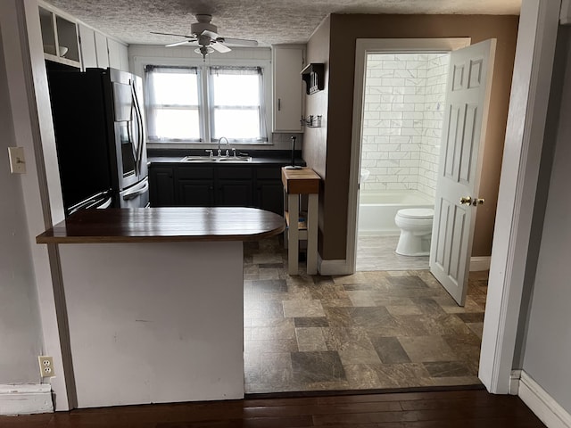 kitchen with stainless steel refrigerator with ice dispenser, a breakfast bar, sink, kitchen peninsula, and ceiling fan