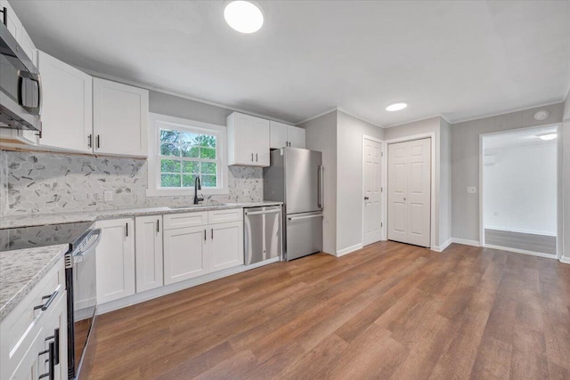 kitchen featuring light wood finished floors, stainless steel appliances, backsplash, ornamental molding, and a sink