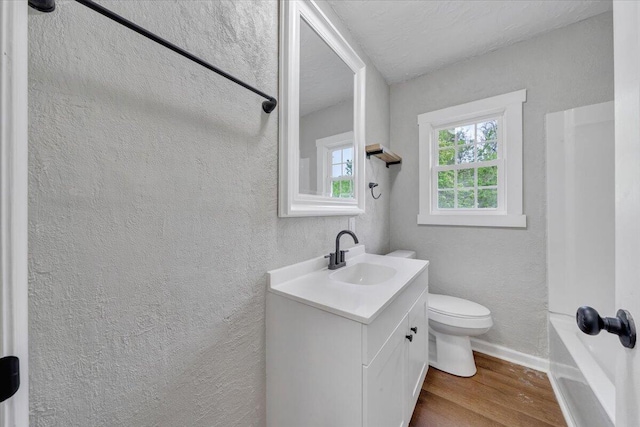 bathroom with toilet, baseboards, wood finished floors, a textured wall, and vanity