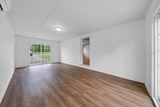 unfurnished room featuring baseboards, wood finished floors, and an AC wall unit