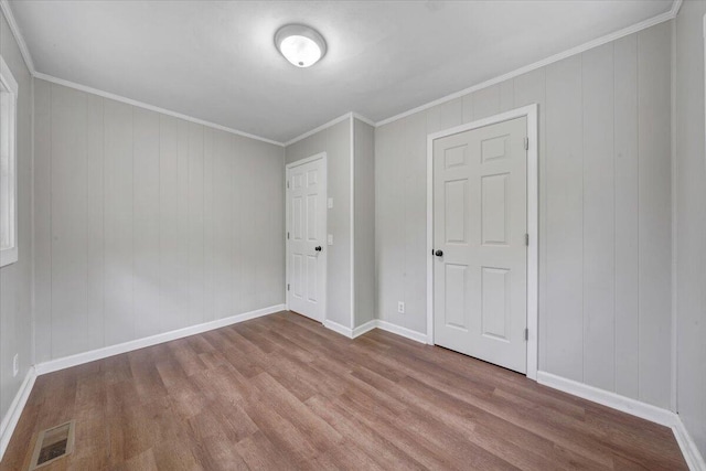 unfurnished bedroom featuring baseboards, wood finished floors, visible vents, and crown molding