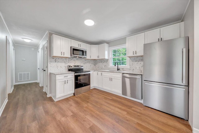 kitchen featuring tasteful backsplash, appliances with stainless steel finishes, light wood finished floors, white cabinetry, and visible vents