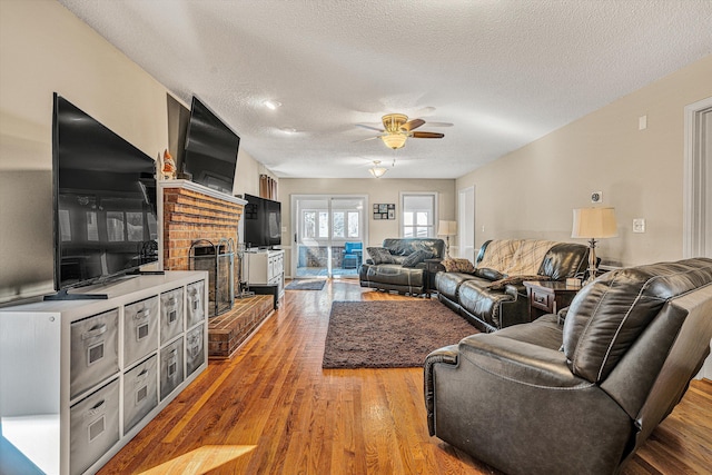 living room with hardwood / wood-style flooring, a fireplace, a textured ceiling, and ceiling fan