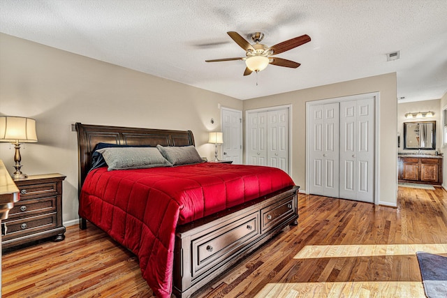 bedroom featuring hardwood / wood-style floors, ceiling fan, two closets, and a textured ceiling