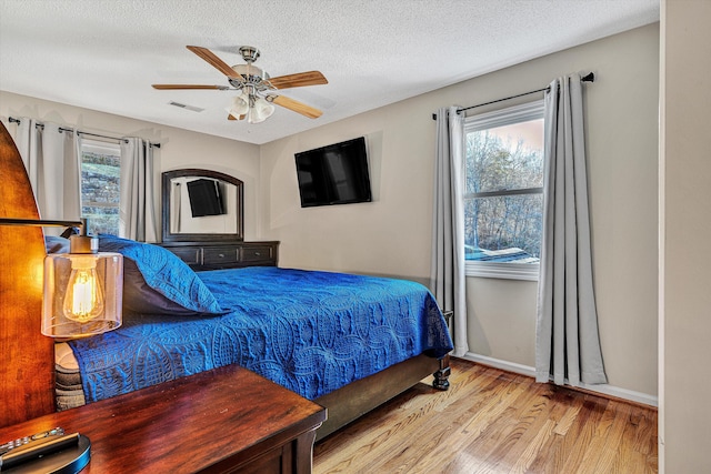 bedroom with ceiling fan, a textured ceiling, and light hardwood / wood-style flooring