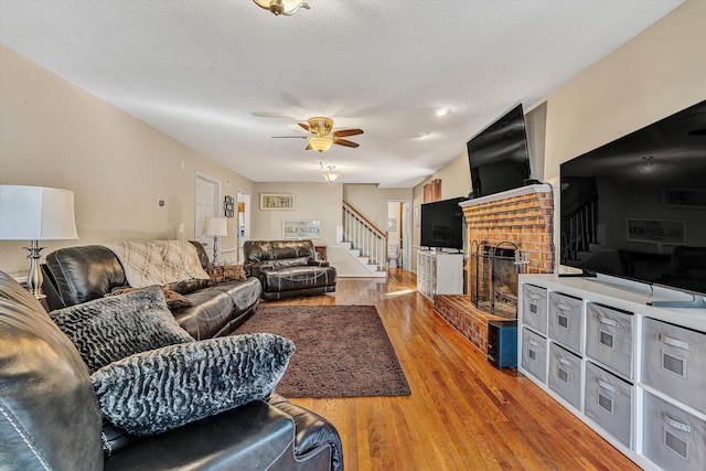 living room featuring wood-type flooring, a brick fireplace, ceiling fan, and a textured ceiling