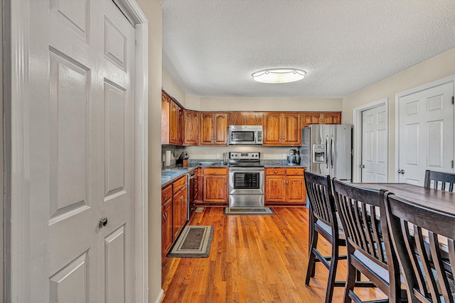 kitchen with light hardwood / wood-style floors, a textured ceiling, and appliances with stainless steel finishes