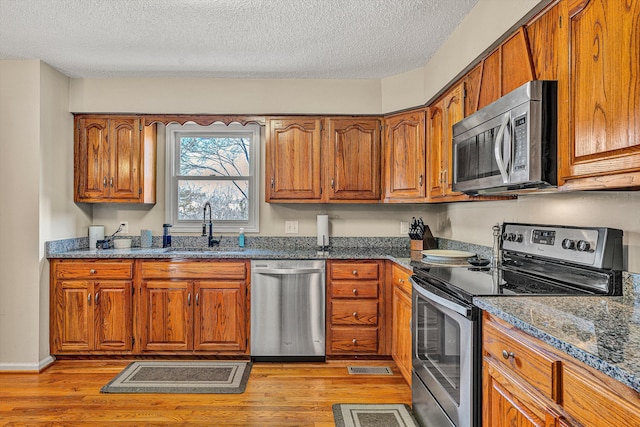 kitchen with sink, dark stone countertops, light wood-type flooring, stainless steel appliances, and a textured ceiling