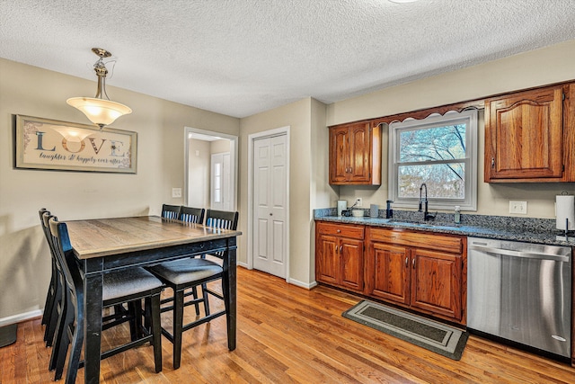 kitchen featuring decorative light fixtures, sink, stainless steel dishwasher, a textured ceiling, and light hardwood / wood-style flooring