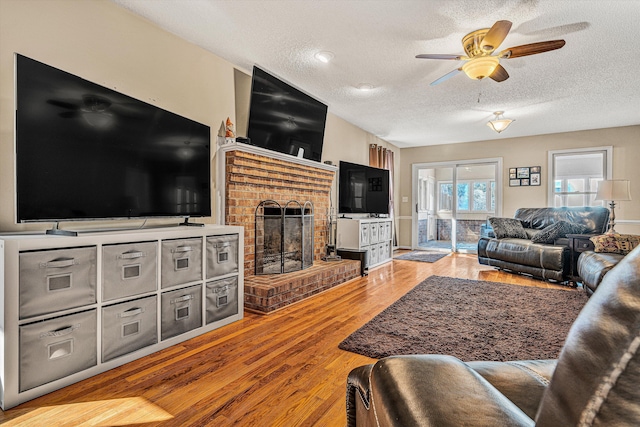 living room featuring wood-type flooring, a textured ceiling, ceiling fan, and a fireplace