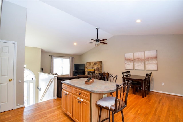 kitchen featuring lofted ceiling, light hardwood / wood-style flooring, a kitchen breakfast bar, a fireplace, and a kitchen island