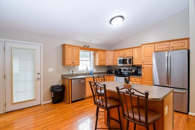 kitchen featuring lofted ceiling, a breakfast bar area, light wood-type flooring, appliances with stainless steel finishes, and a kitchen island