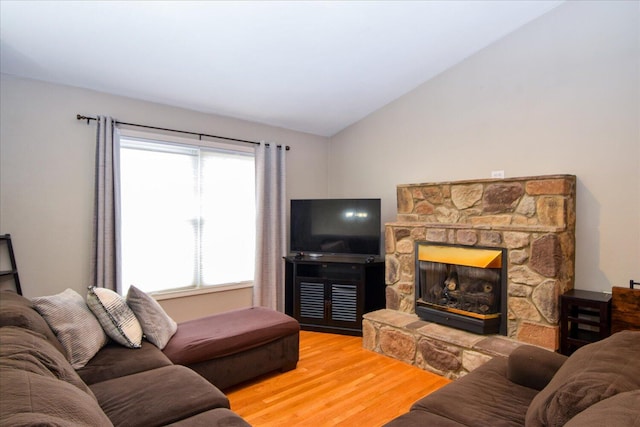 living room featuring vaulted ceiling, a stone fireplace, and hardwood / wood-style floors