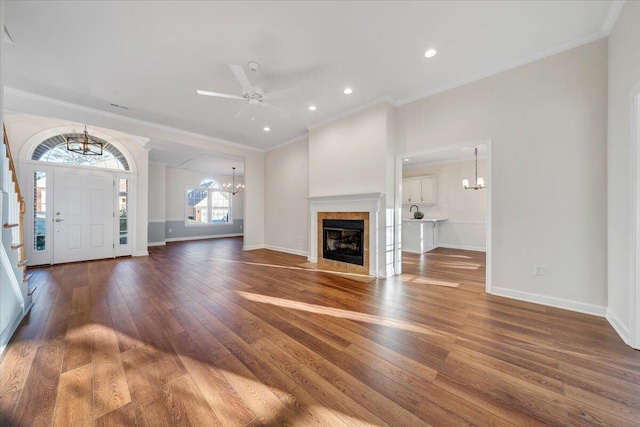 unfurnished living room featuring ornamental molding, ceiling fan with notable chandelier, dark wood-type flooring, and a tile fireplace