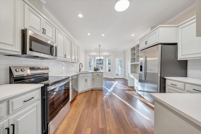 kitchen featuring sink, crown molding, decorative light fixtures, stainless steel appliances, and white cabinets