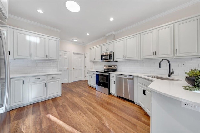 kitchen featuring appliances with stainless steel finishes, white cabinetry, sink, ornamental molding, and light hardwood / wood-style flooring