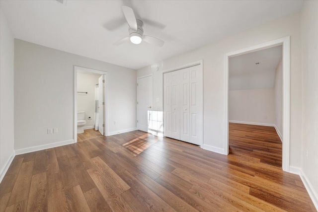 unfurnished bedroom featuring hardwood / wood-style flooring, ceiling fan, ensuite bath, and a closet