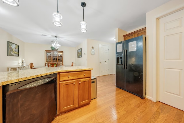 kitchen featuring pendant lighting, light stone countertops, light wood-type flooring, and black appliances