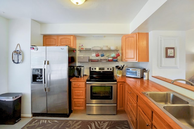 kitchen with appliances with stainless steel finishes, sink, wooden counters, and light tile patterned floors