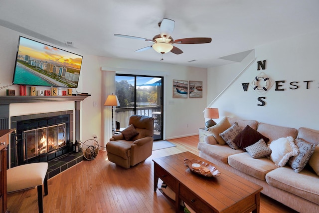 living room with hardwood / wood-style flooring, ceiling fan, and a tiled fireplace