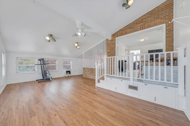 unfurnished living room with light wood-type flooring, ceiling fan, brick wall, and vaulted ceiling