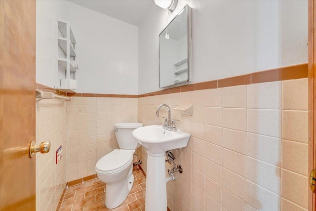 half bath with tile patterned floors, toilet, a sink, tile walls, and wainscoting