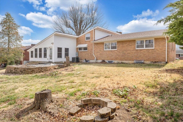 rear view of property with central air condition unit, a fire pit, brick siding, and a yard