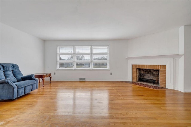 living area featuring visible vents, baseboards, light wood-style flooring, and a fireplace