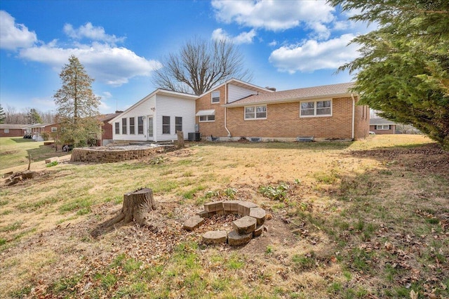 rear view of house with cooling unit, a lawn, brick siding, and an outdoor fire pit