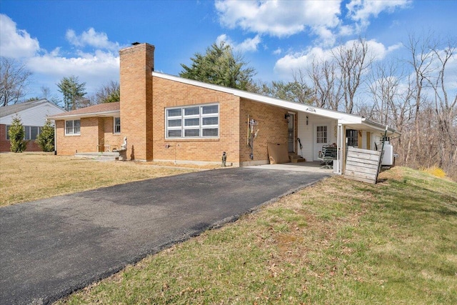 ranch-style house featuring brick siding, aphalt driveway, a carport, and a front lawn