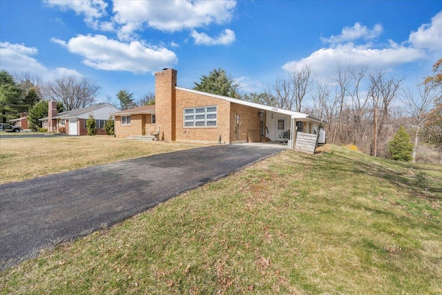 ranch-style house featuring an attached carport, a front yard, driveway, and a chimney