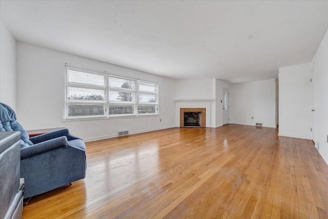 living room featuring a brick fireplace, baseboards, visible vents, and light wood finished floors
