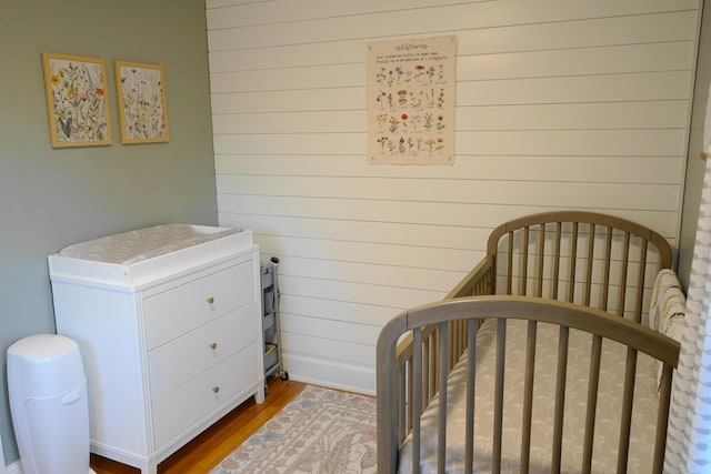 bedroom featuring a nursery area, wood-type flooring, and wood walls