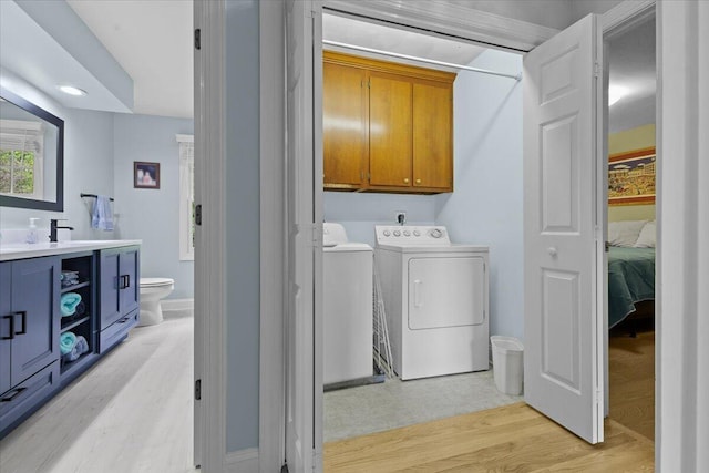 clothes washing area featuring light hardwood / wood-style floors, sink, washing machine and dryer, and cabinets