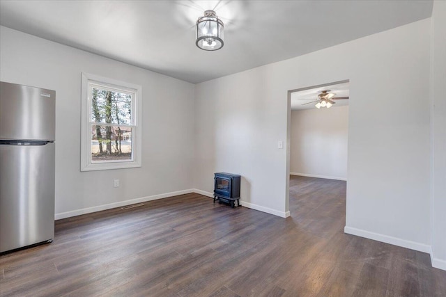 interior space featuring a wood stove, dark wood-type flooring, and ceiling fan