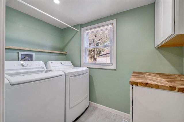 clothes washing area with washer and dryer, light hardwood / wood-style floors, and cabinets