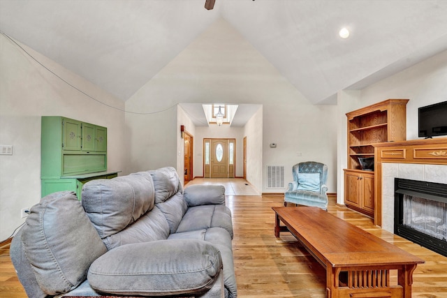 living room featuring high vaulted ceiling, a tile fireplace, and light wood-type flooring