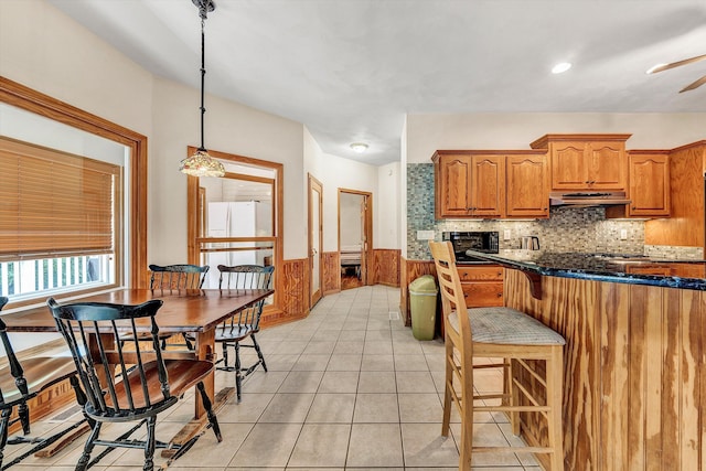 kitchen featuring light tile patterned flooring, decorative light fixtures, dark stone countertops, backsplash, and white refrigerator