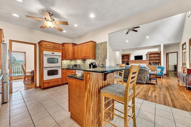 kitchen with a kitchen bar, light tile patterned floors, ceiling fan, kitchen peninsula, and stainless steel appliances