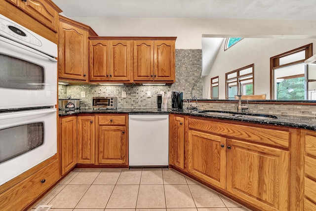 kitchen featuring sink, white appliances, light tile patterned floors, tasteful backsplash, and dark stone counters