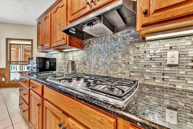 kitchen featuring light tile patterned floors, dark stone countertops, tasteful backsplash, custom range hood, and stainless steel gas stovetop