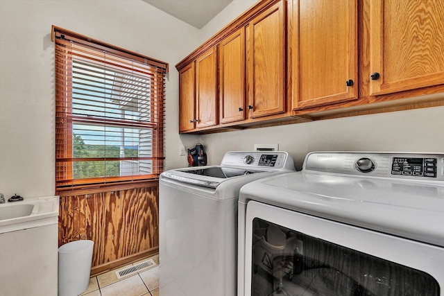 clothes washing area featuring cabinets, washing machine and dryer, and light tile patterned flooring