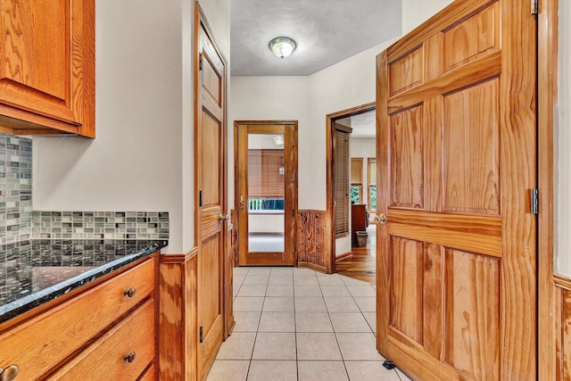 kitchen featuring tasteful backsplash, light tile patterned floors, dark stone counters, and wood walls