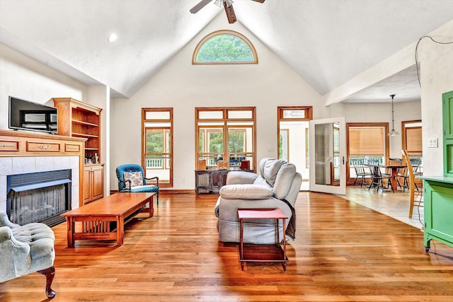 living room featuring ceiling fan, a fireplace, high vaulted ceiling, and light wood-type flooring