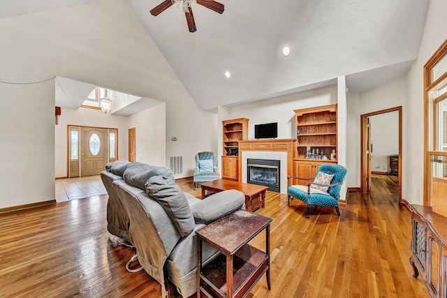 living room featuring ceiling fan, high vaulted ceiling, a tiled fireplace, and light hardwood / wood-style floors