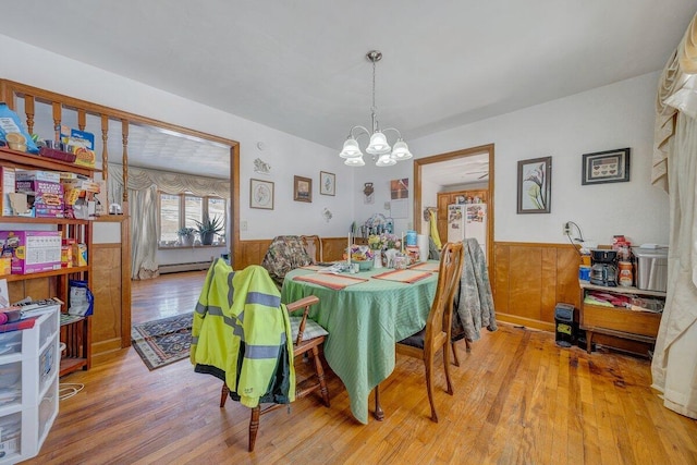 dining room featuring a wainscoted wall, a baseboard radiator, an inviting chandelier, wood walls, and wood finished floors