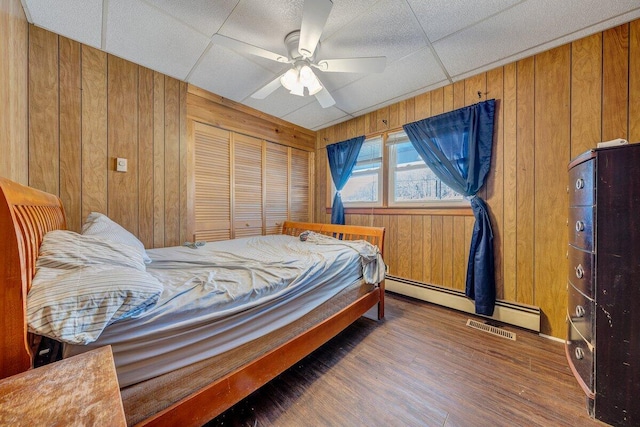 bedroom with visible vents, baseboard heating, a ceiling fan, wood walls, and wood finished floors