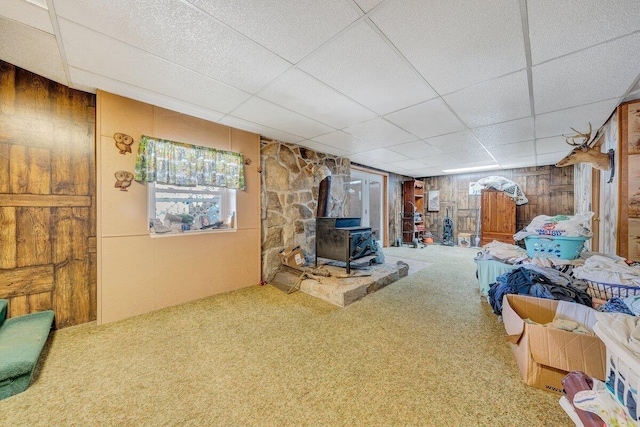 interior space with carpet floors, a paneled ceiling, a wood stove, and wooden walls